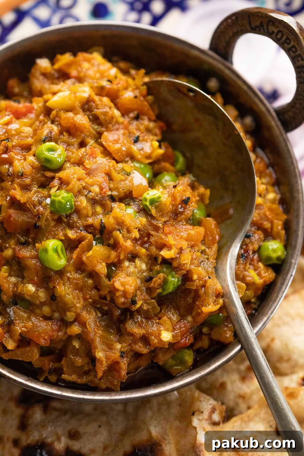 Baingan Bharta served in a traditional copper kadhai with tandoori roti and sliced onions on the side, beautifully garnished with fresh coriander. A complete Indian meal setup.