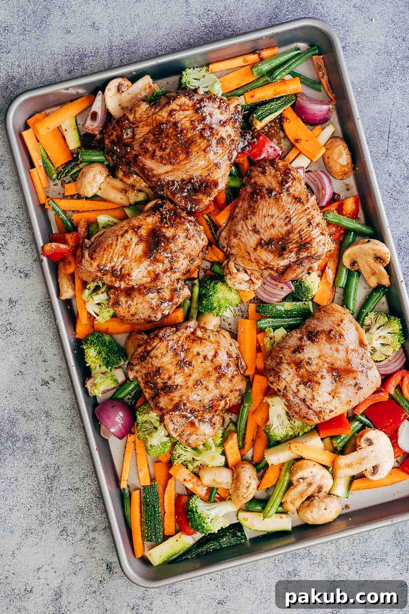 Marinated sheet pan honey balsamic chicken thighs with veggies on a baking tray ready to go into the oven