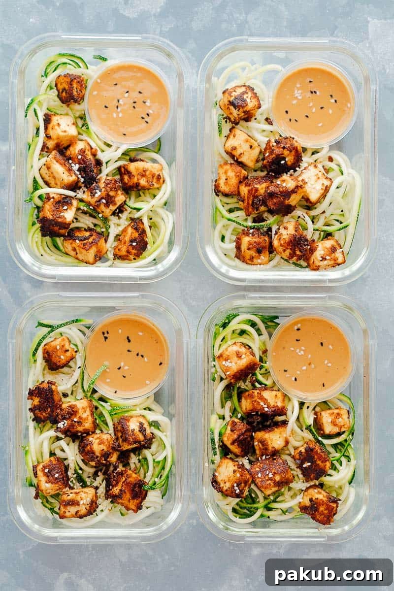 Four meal prep containers filled with crispy sesame tofu and zucchini noodles, ready to eat.