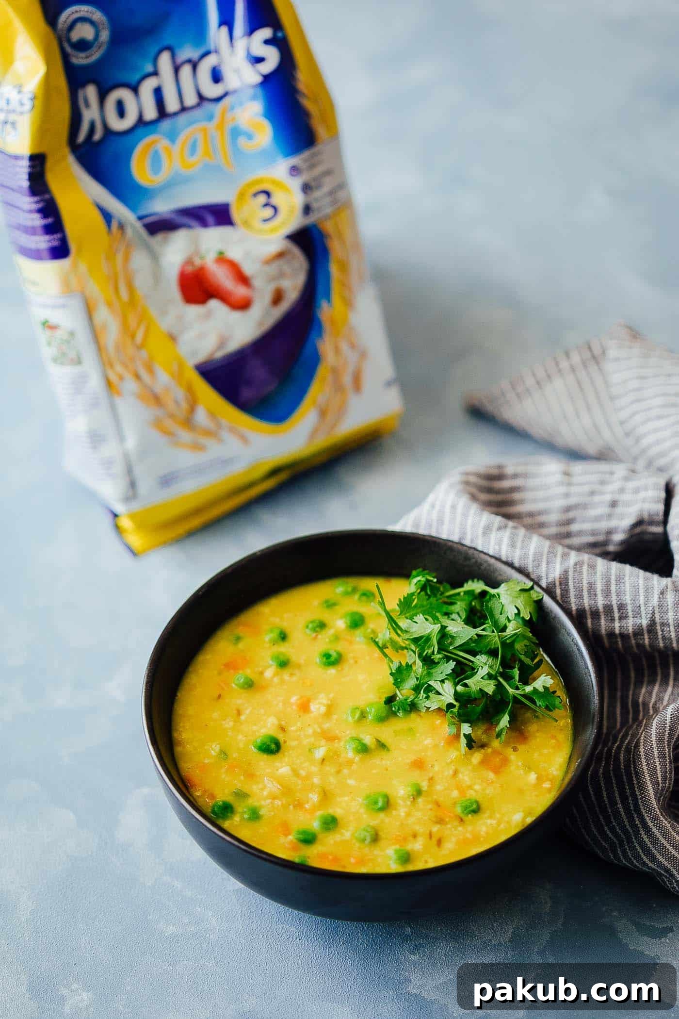 Beyond Sweet: 5 Savory Oatmeal Breakfast Recipes 5 A healthy and hearty oats khichdi, an Indian savory porridge, packed with vegetables, served in a bowl with a spoon and garnished.