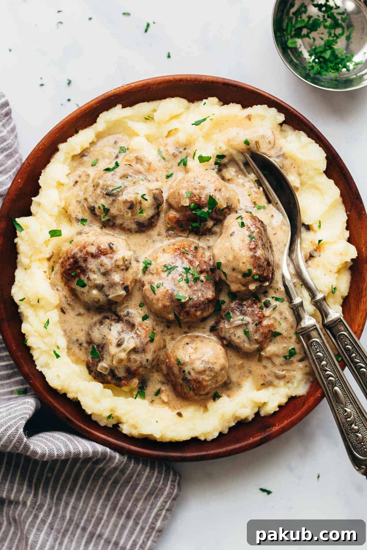 Creamy chicken meatballs in mushroom sauce served over mashed potatoes in a bowl, garnished with herbs