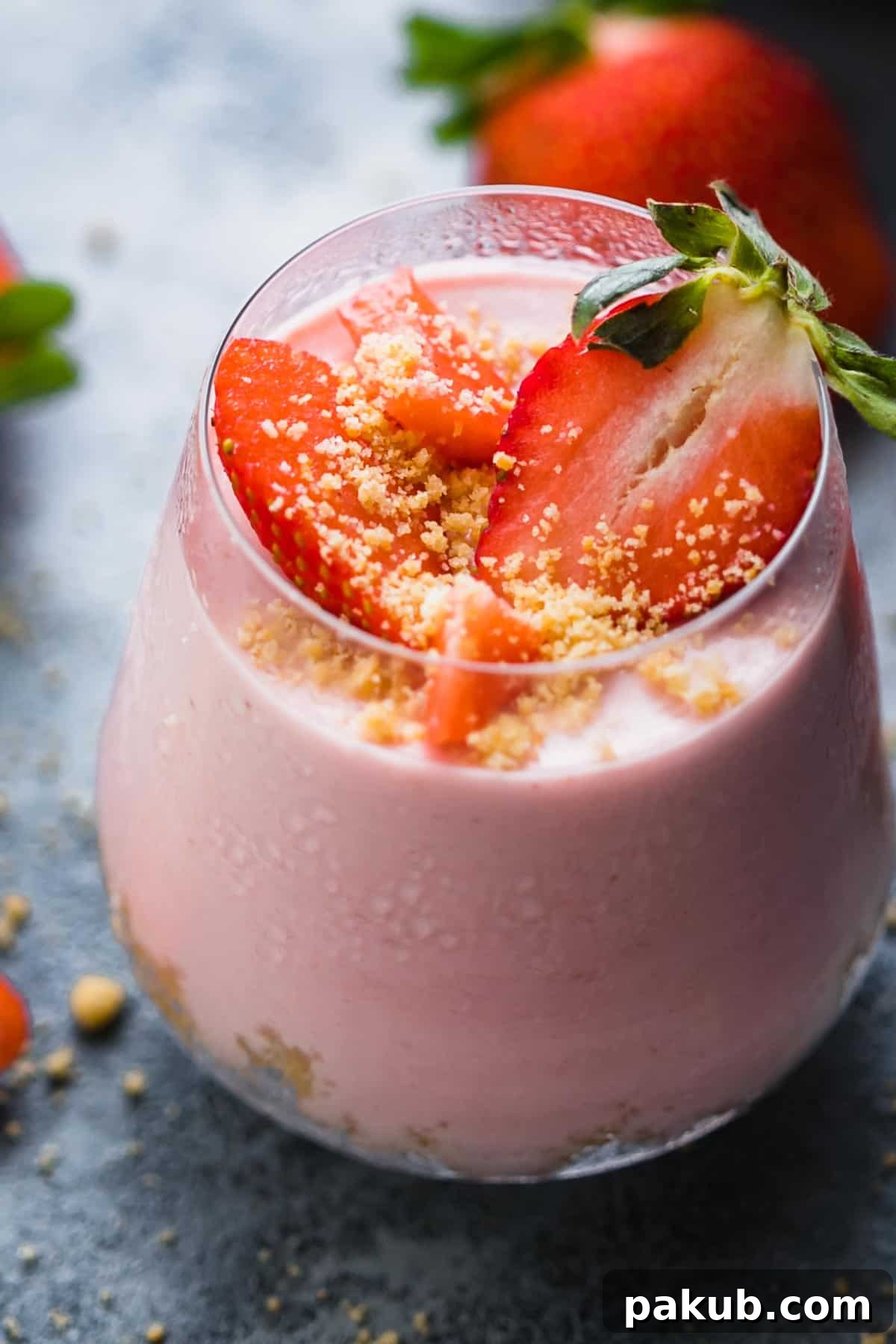 No Fuss Strawberry Cheesecake Jars 7 A close-up view of a beautifully garnished No-Bake Strawberry Cheesecake Jar, topped with vibrant fresh strawberry slices and a sprinkle of golden biscuit crumbs, ready to be enjoyed.