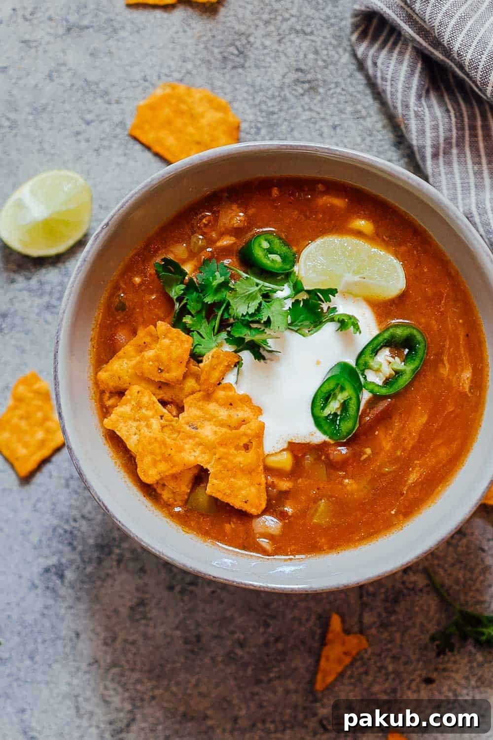 Instant Pot Chicken Enchilada Soup: A fast, thick, and spicy recipe loaded with chicken, beans, and corn, topped with sour cream and cilantro for ultimate comfort. A vibrant bowl of Instant Pot Chicken Enchilada Soup, garnished generously with cool sour cream, fresh cilantro, thinly sliced jalapeños, crispy tortilla chips, and a zesty lime wedge, showcasing its rich texture and appealing presentation.