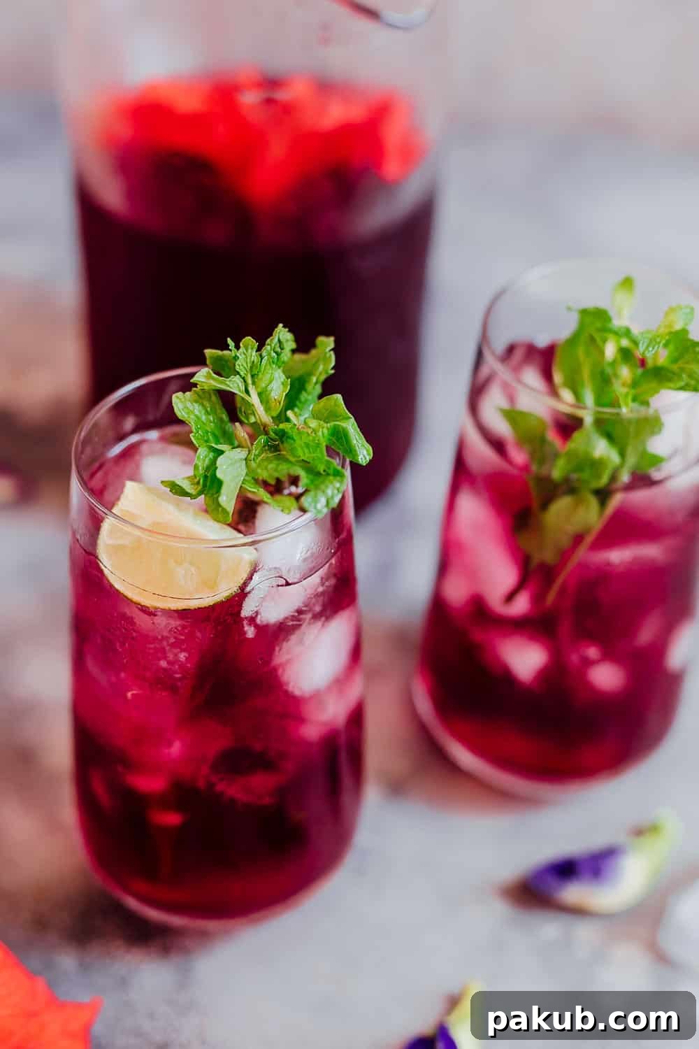 Closeup of a glass of hibiscus tea with ice cubes, mint and lemon