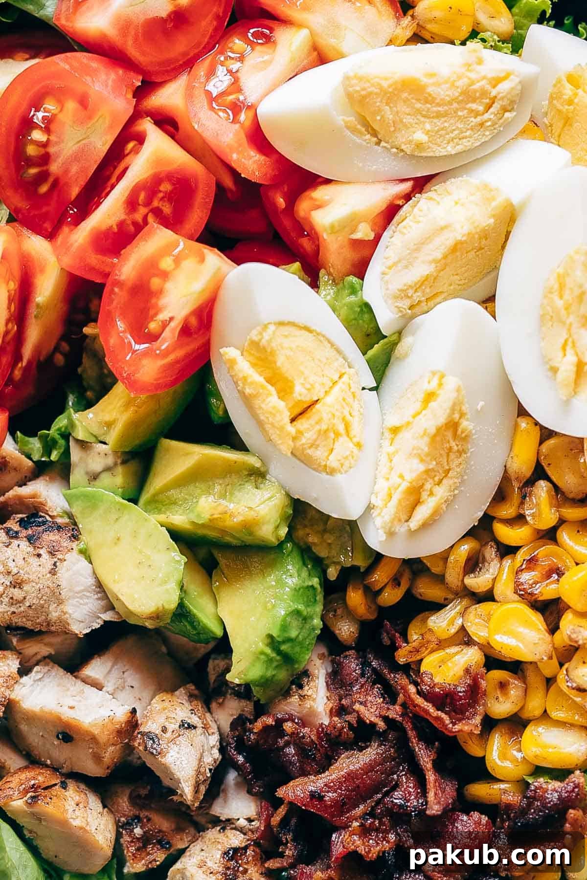 A wholesome and filling Chicken Cobb Salad, demonstrating how simple, fresh ingredients combine to create a deeply satisfying meal for any occasion. Another perspective of the assembled Chicken Cobb Salad in a bowl, showcasing the generous portions of grilled chicken, crispy bacon, boiled eggs, sweet corn, and ripe tomatoes, ready to be dressed.