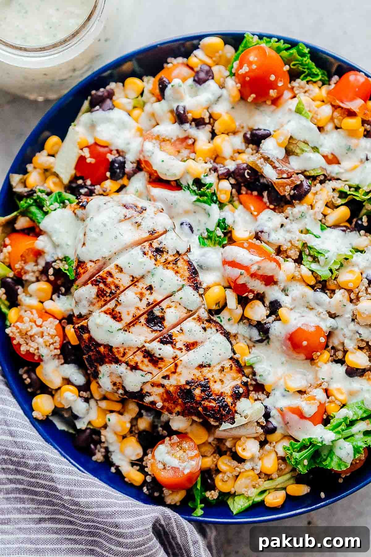 Hearty Southwest Chicken Quinoa Bean Salad in a blue bowl, drizzled with creamy cilantro yogurt dressing.
