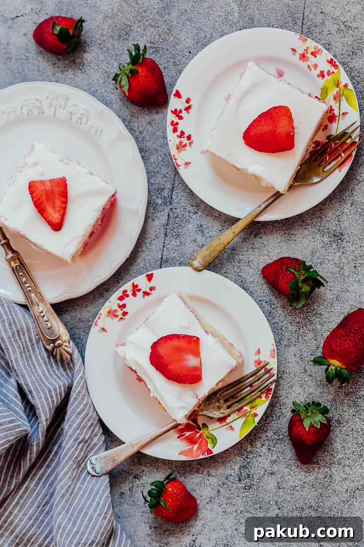 This homemade strawberry poke cake is soft, moist, and infused with jello, topped with whipped cream and fresh strawberries. It's an easy, elegant dessert perfect for holidays like Easter or Mother's Day, or just a delightful pink treat. Three perfectly sliced portions of homemade strawberry poke cake, served on elegant white plates with forks, garnished with fresh whole strawberries on the side. The cake layers show the beautiful pink jello infusion.
