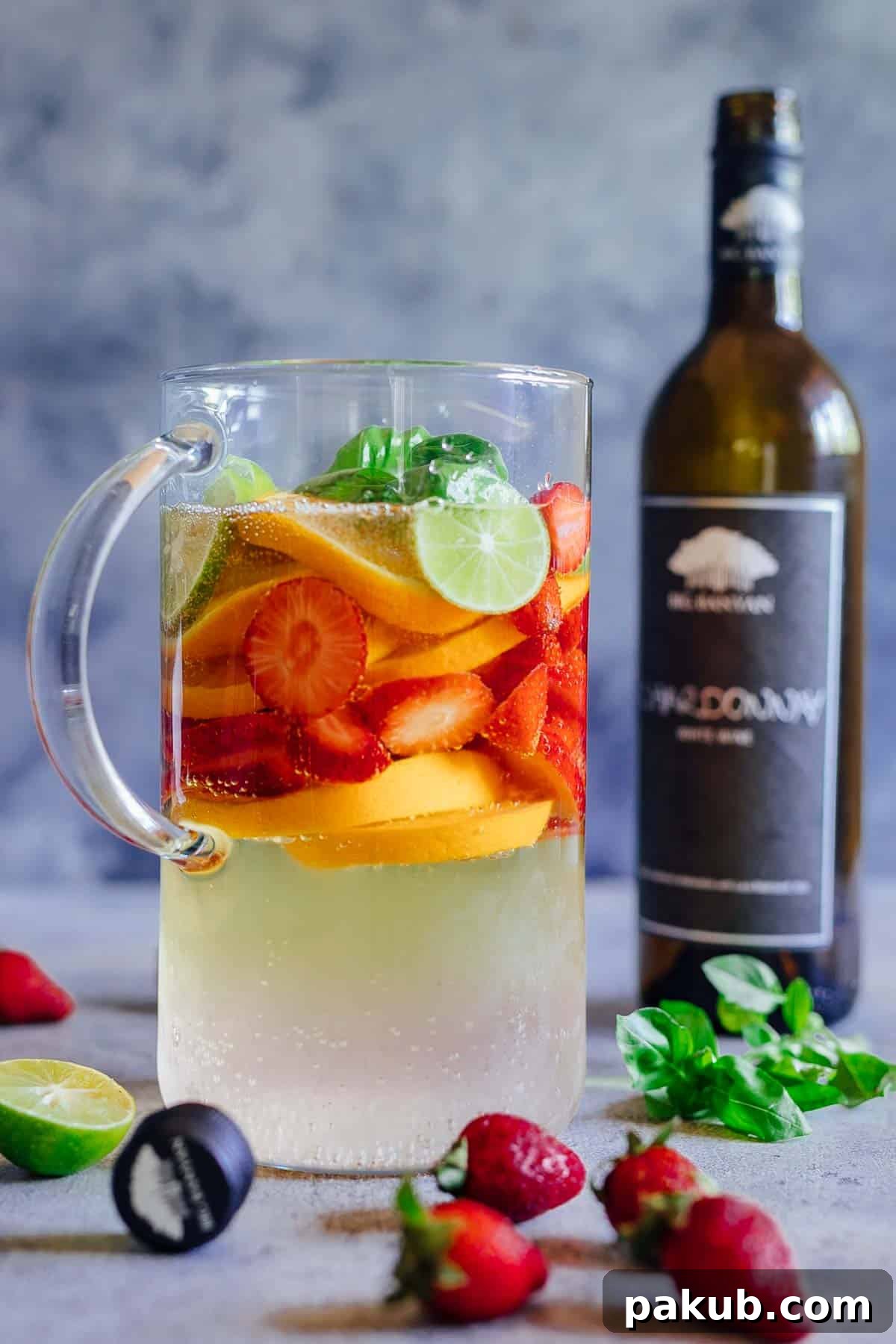 A pitcher of strawberry orange white wine sangria with a bottle of chardonnay in the background, hinting at the wine used