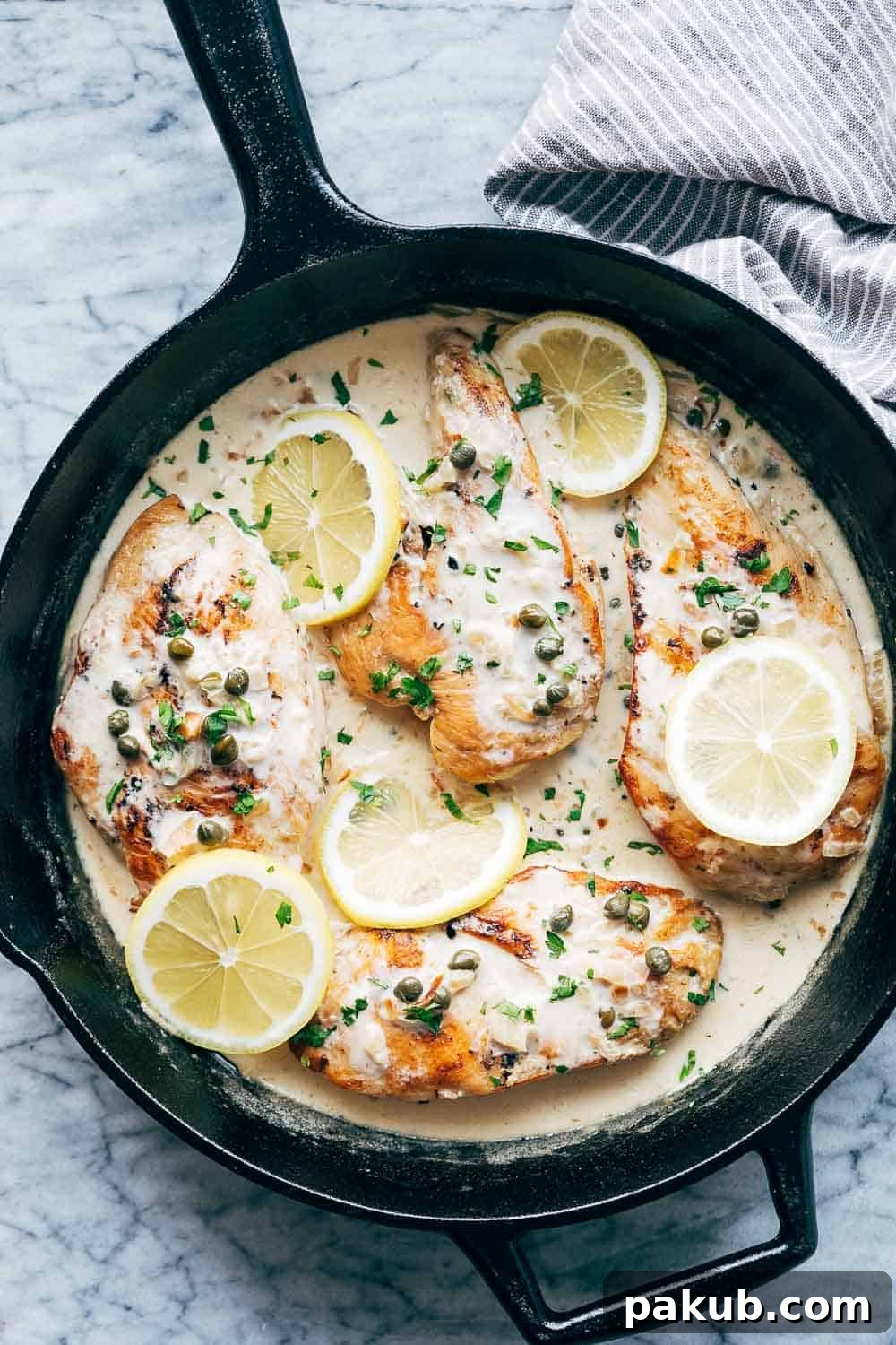 Creamy lemon chicken scallopini served in a cast iron skillet with four chicken breasts, garnished with capers and fresh lemon slices.