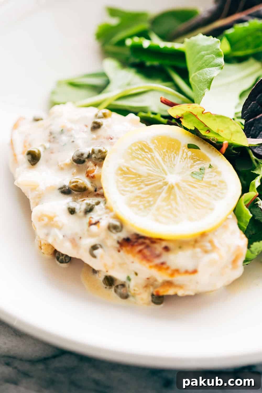 Creamy lemon chicken scallopini served elegantly with a side of fresh, light salad in a white bowl.