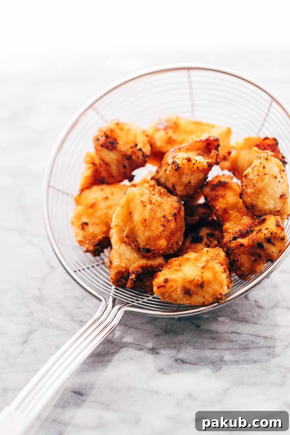 KOREAN POPCORN CHICKEN is sticky, spicy, tangy and crunchy. Inspired by the hyper-famous Korean street snack, Dakgangjeong, boneless chicken is deep fried and tossed in a sweet, sour and spicy sauce that makes every bite super addictive. #chicken #appetizer #party #snack #recipe Fried golden crunchy chicken in a frying sieve