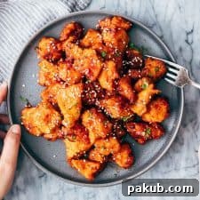K-Style Crispy Chicken Poppers 2 Korean Popcorn Chicken on a plate with a hand coming up to take a bite with a fork