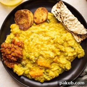 Khichdi served on a black plate with papad, tomato chutney and aloo fry