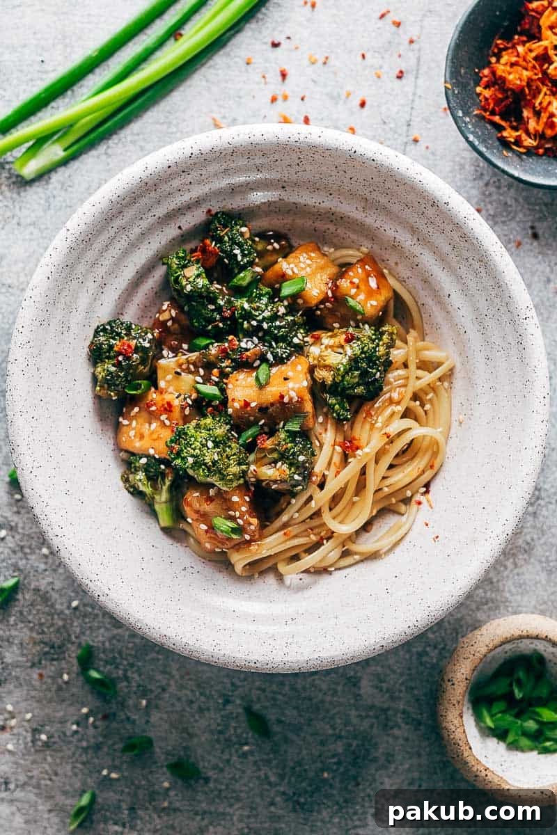 Crispy tofu broccoli stir fry in a white bowl topped with chilli flakes, green onions and sesame seeds