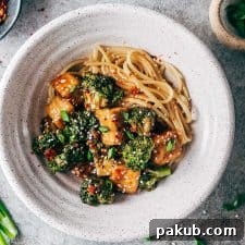 Crispy tofu broccoli stir fry in a white bowl topped with chilli flakes, green onions and sesame seeds.