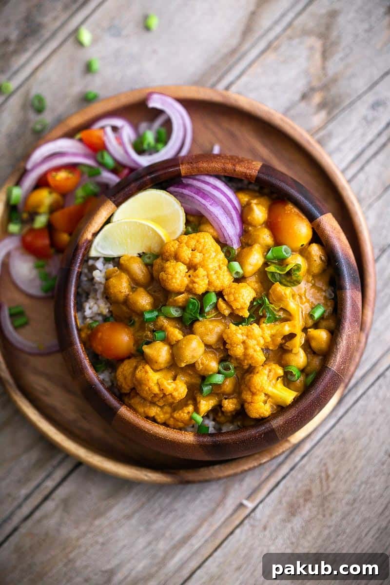 Enjoy a hearty bowl of cauliflower chickpea coconut curry, beautifully garnished with fresh lime and onions, perfect for a fulfilling and comforting meal at home. #currynight #healthyeating #comfortfood #homecooking #dinnerideas A serving of homemade Cauliflower Chickpea Coconut Curry in a rustic brown bowl, garnished with fresh onions and lime wedges, ready to be enjoyed as a wholesome and satisfying meal.