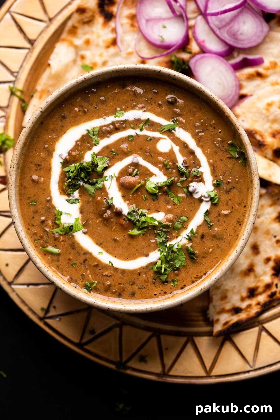 Dal Makhani Mastery Stovetop Pressure Cooker Instant Pot 6 Dal Makhani served in a rustic brown ceramic bowl with a generous swirl of fresh cream on top, accompanied by soft butter garlic naan and refreshing sliced onions on the side.