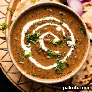 Dal Makhani served in a brown ceramic bowl with cream drizzled on top, accompanied by naan and sliced onions, highlighting the dish's visual appeal.