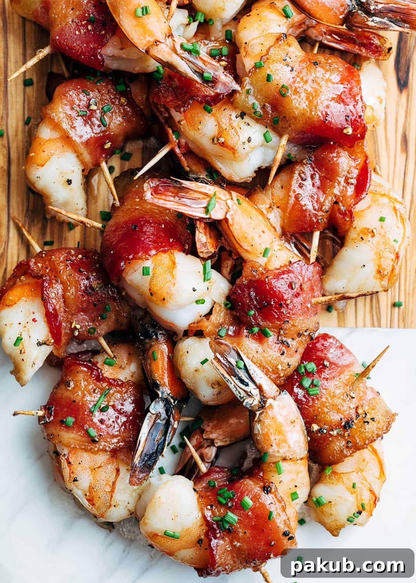 15 Bacon Creations to Make Every Meal a Party 13 An enticing pile of Bacon Wrapped Shrimp, artfully arranged on a marble and wooden serving board, complete with toothpicks for easy serving. Each shrimp is perfectly wrapped in crispy bacon.