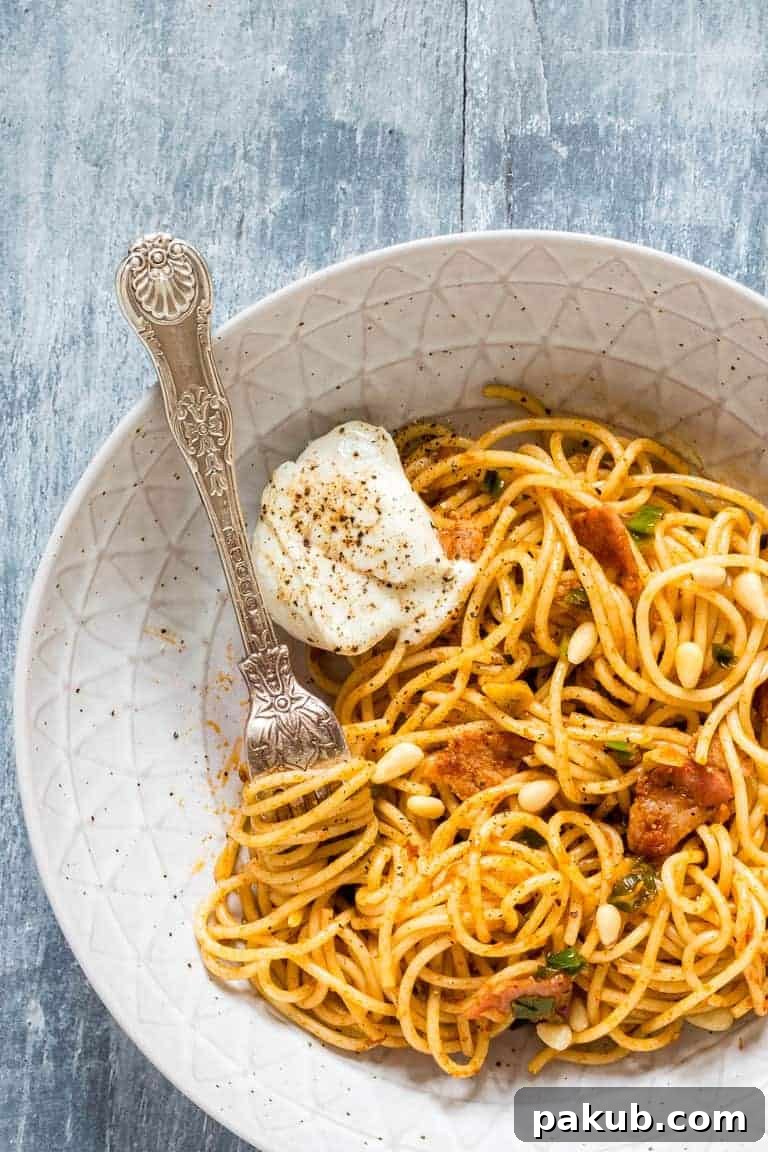 15 Bacon Creations to Make Every Meal a Party 16 A mouth-watering close-up of vibrant Garlic Harissa Bacon Pasta, served in a clean white bowl, highlighting the colorful sauce, pasta strands, and crispy bacon.