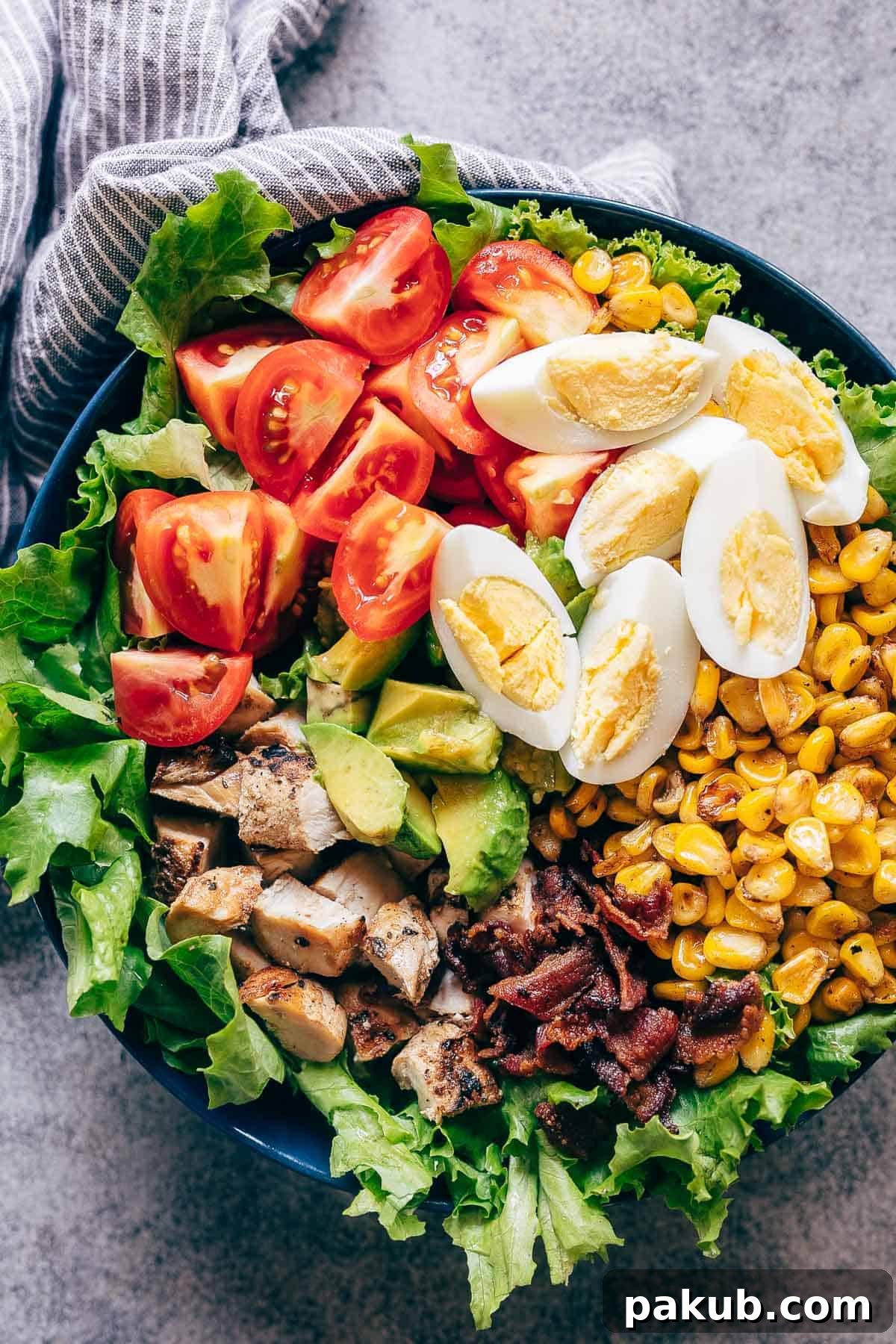 15 Bacon Creations to Make Every Meal a Party 3 A beautifully presented Chicken Cobb Salad in a bowl, featuring crisp lettuce, juicy tomatoes, grilled chicken, savory bacon, sweet corn, and perfectly boiled eggs, all ready to be drizzled with dressing.