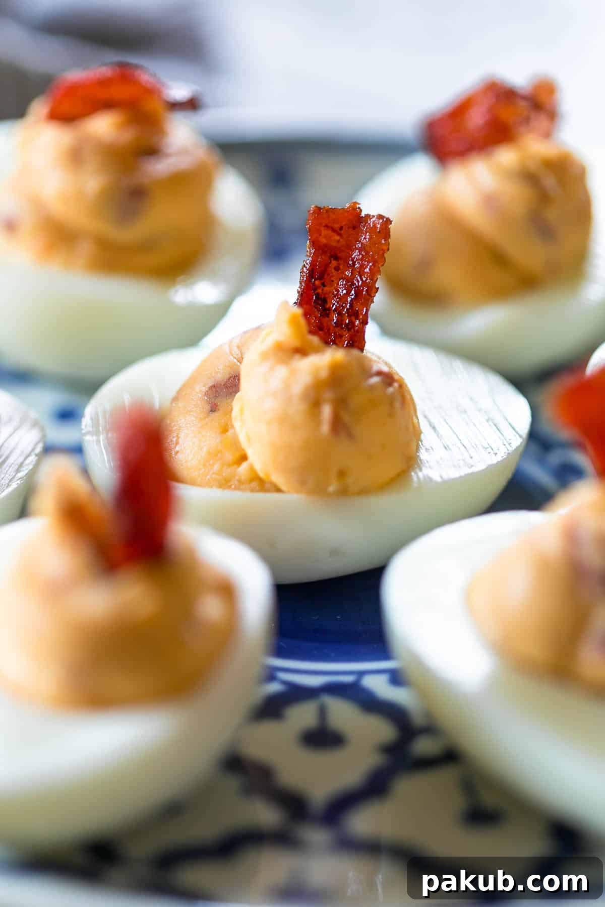 15 Bacon Creations to Make Every Meal a Party 4 Close-up of vibrant Spicy Bacon Deviled Eggs elegantly arranged on a blue and white plate, generously topped with crispy bacon crumbles for an irresistible finish.