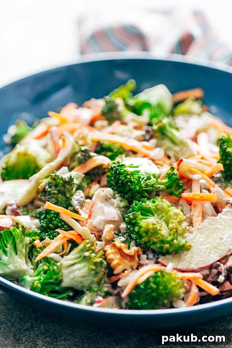 Close-up view of Creamy Apple Broccoli Walnut Salad, showcasing the rich texture of the creamy dressing coating the fresh ingredients in a blue bowl.