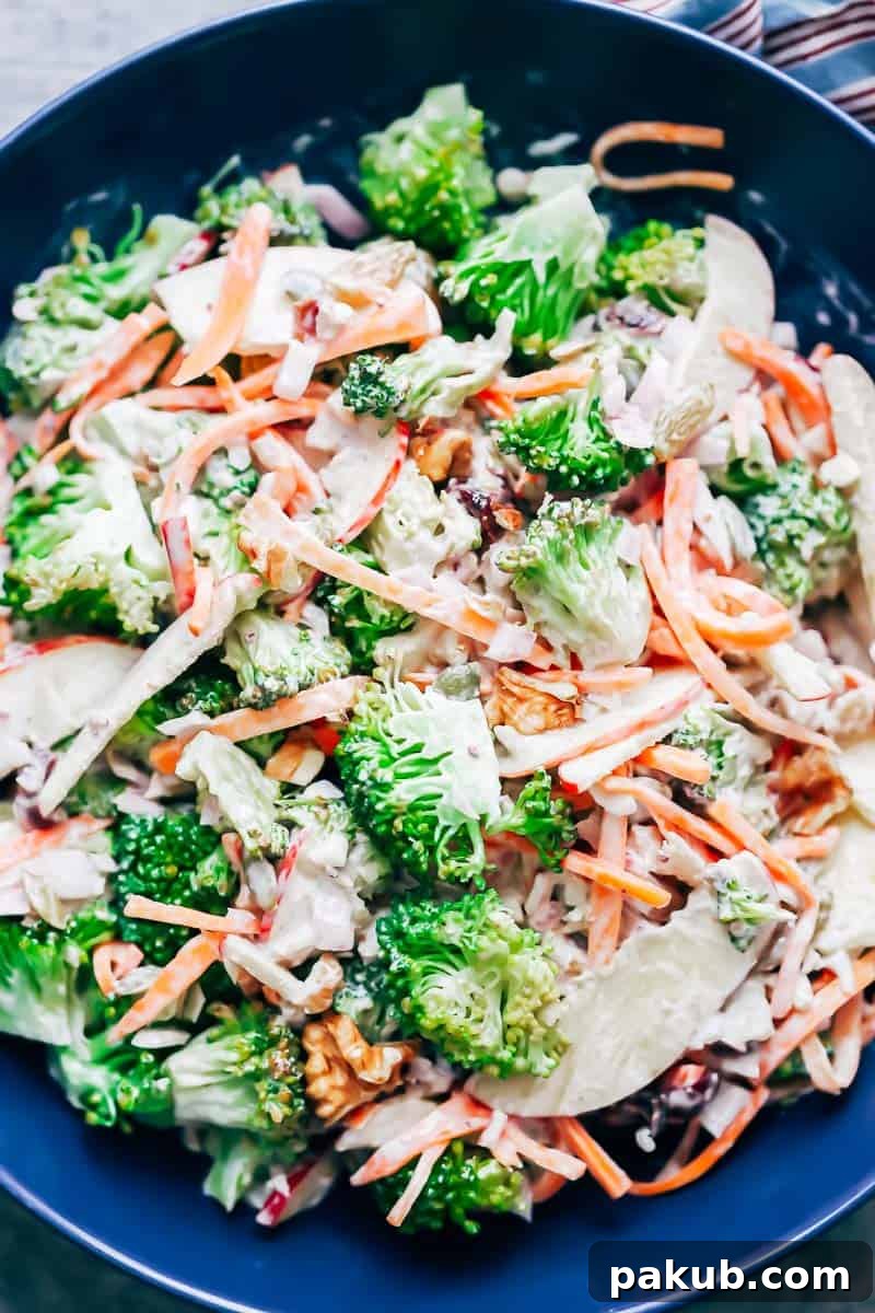 A vibrant display of Creamy Apple Broccoli Walnut Salad, highlighting the bright green broccoli florets, crisp red apple slices, and shredded carrots, all tossed in a creamy dressing.