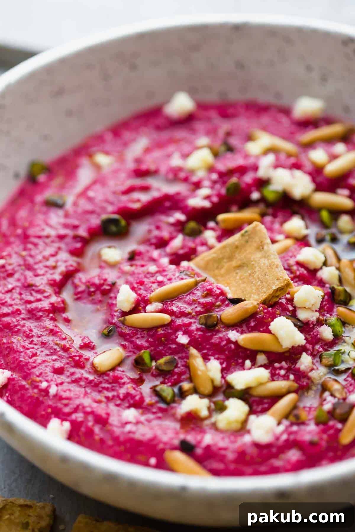Close-up of Egyptian Beetroot Dip in a white speckled bowl, garnished with herbs and nuts.