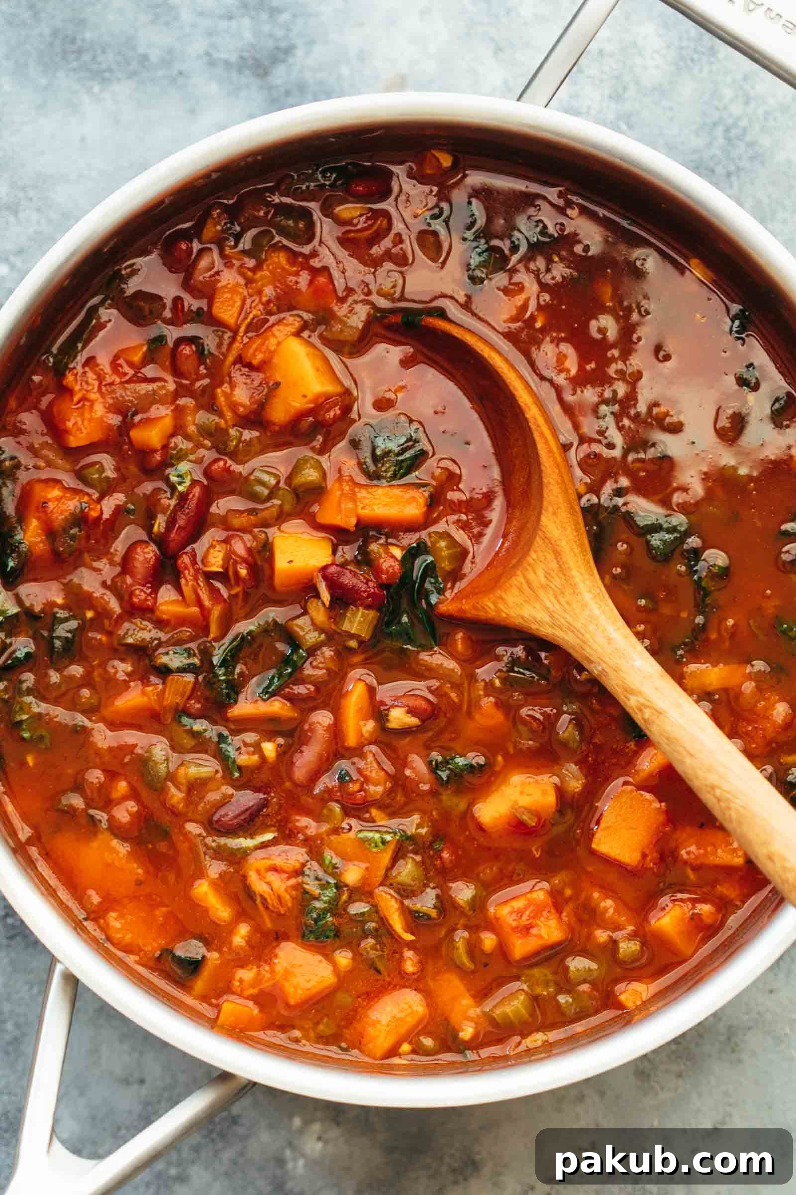 Winter Vegetarian Minestrone Soup straight from the stove in a pot with ladle, rich with vegetables and a vibrant red broth.