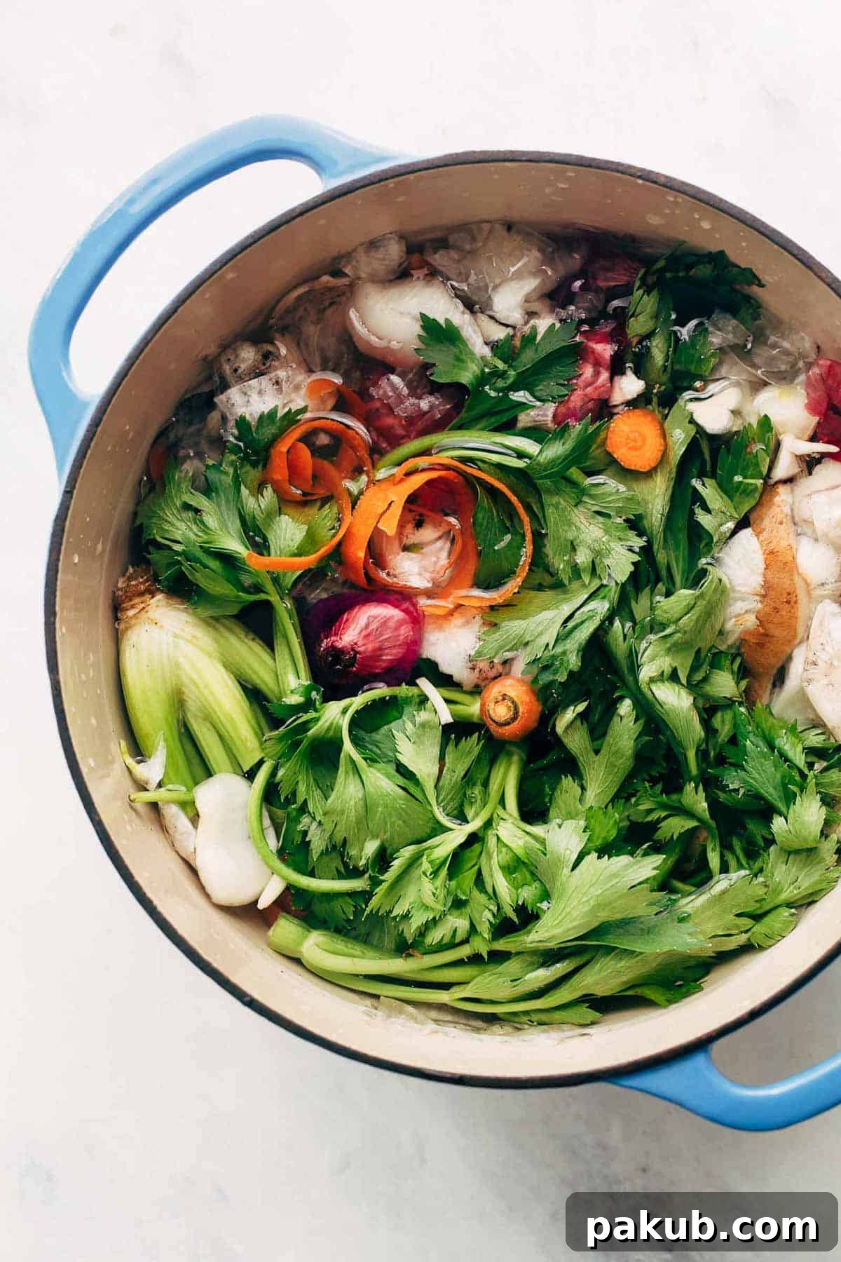 A large pot filled with an assortment of clean vegetable kitchen scraps, fresh herbs, and whole peppercorns, submerged in water, ready to be simmered into homemade vegetable stock.