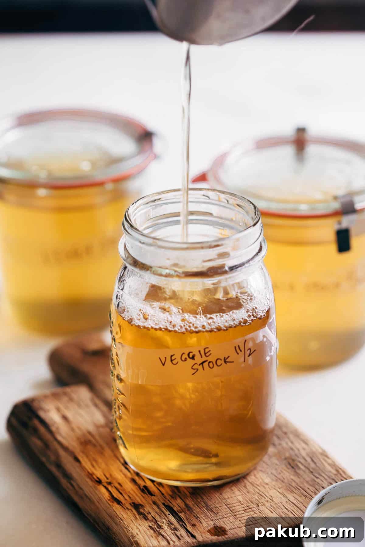 A clear glass canning jar filled with freshly strained, golden homemade vegetable stock, ready for storage or immediate use.