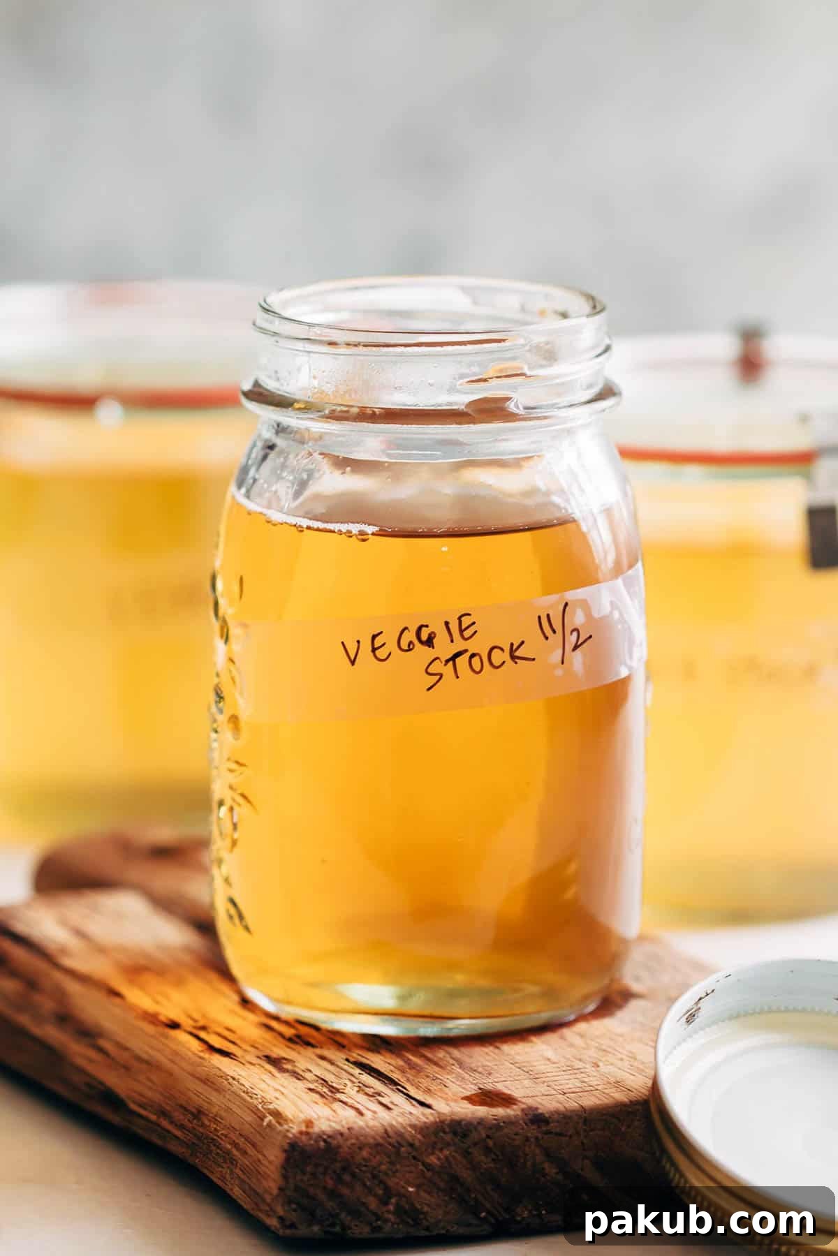 A close-up shot of freshly made vegetable stock, golden and clear, carefully poured into a glass canning jar, ready for use or storage.