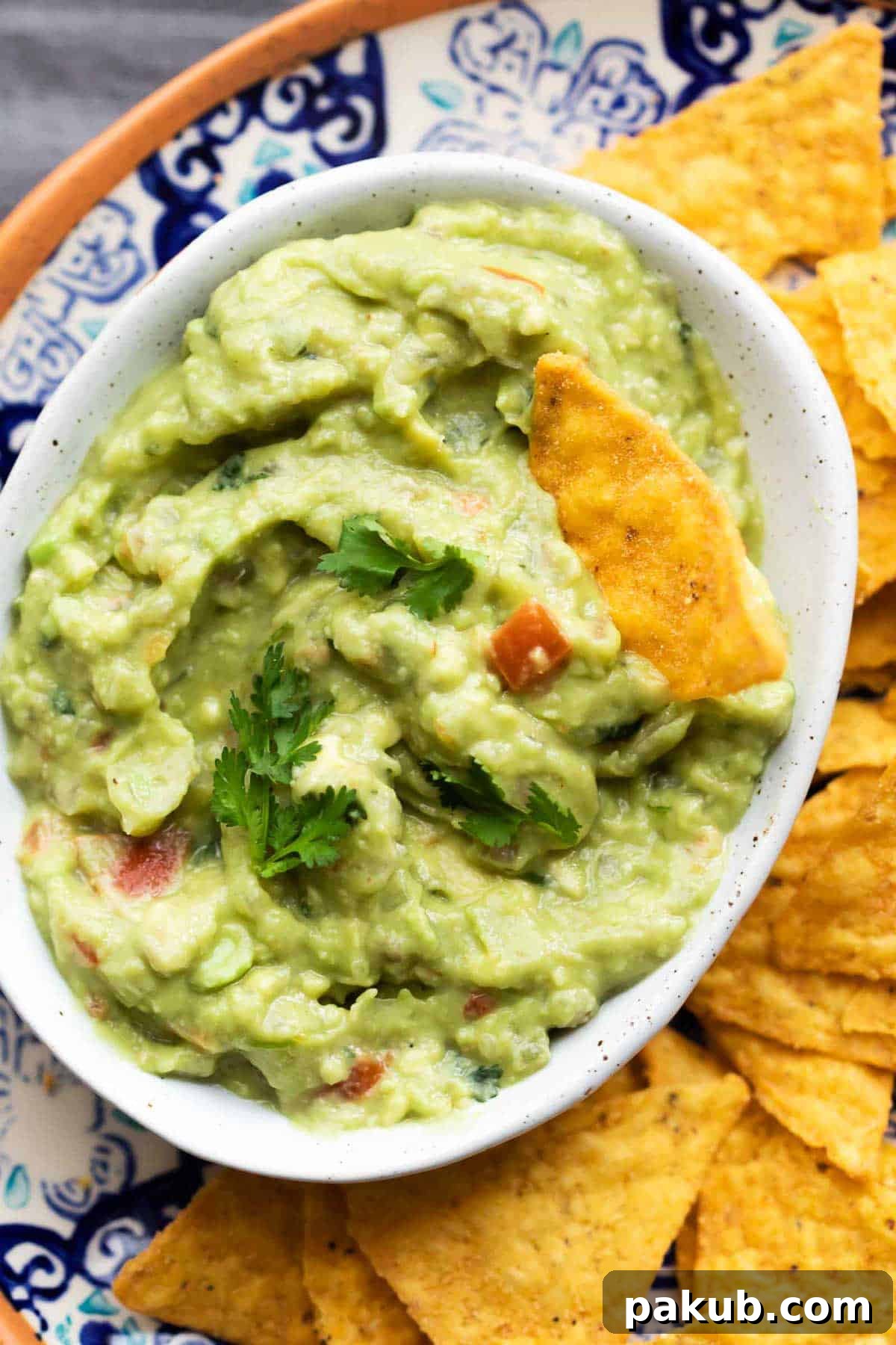 Insanely Delicious Homemade Guacamole 2 Creamy homemade guacamole served in a white bowl, accompanied by a side of crispy tortilla chips, ready for dipping.