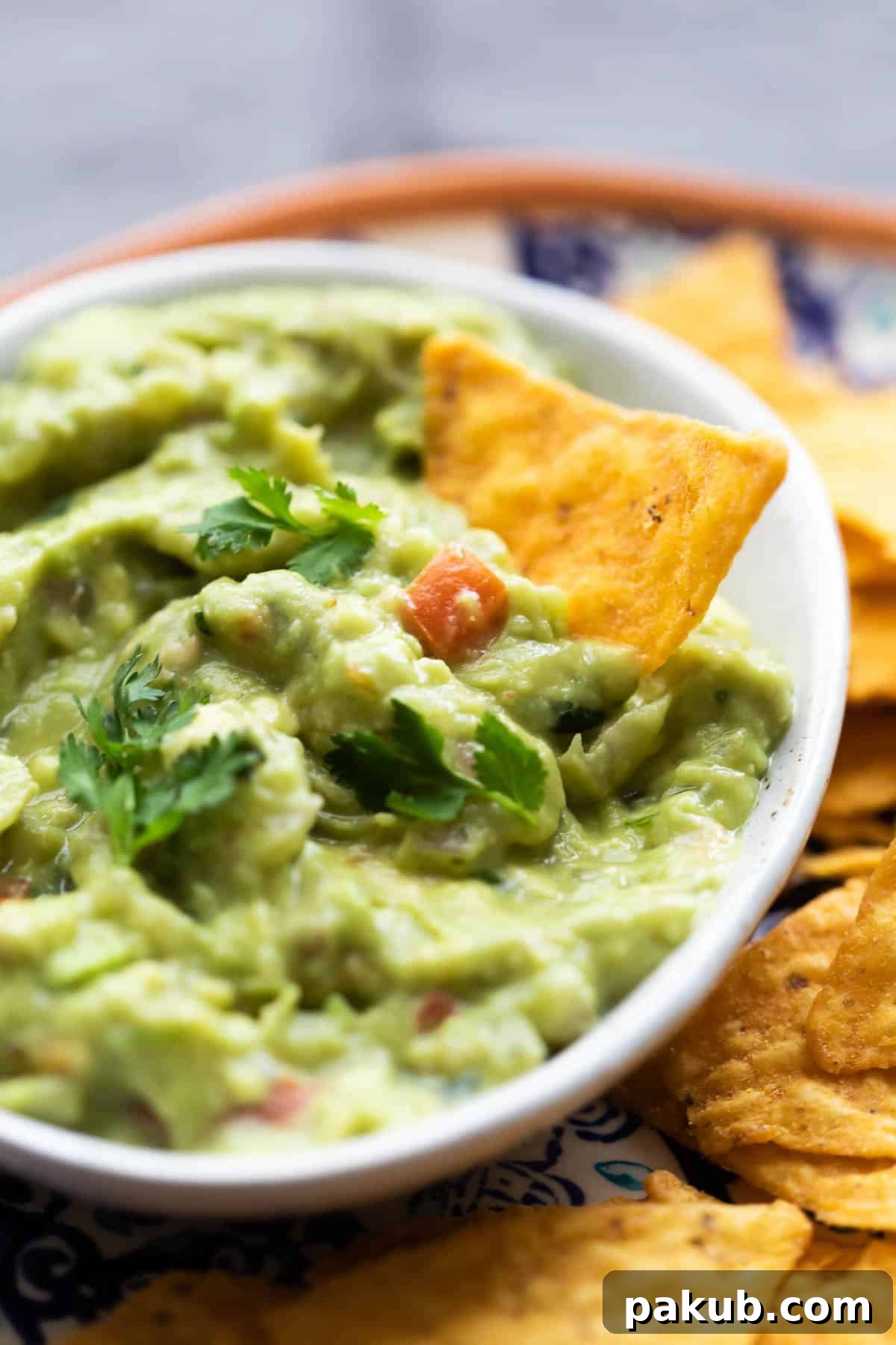 Insanely Delicious Homemade Guacamole 3 Close-up view of vibrant homemade guacamole in a white bowl, with a single tortilla chip already dipped in, showcasing its creamy texture.