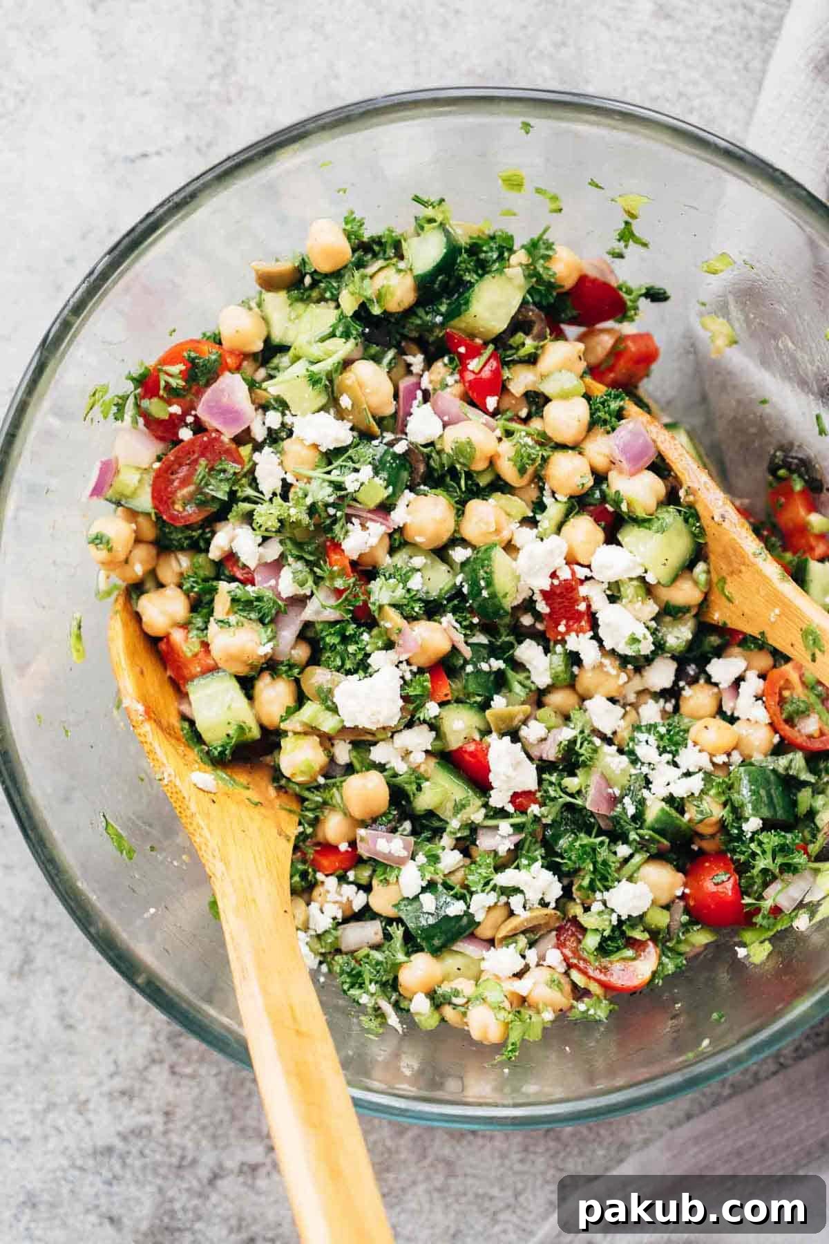 Easy Mediterranean Chickpea Salad tossed in a bowl with two wooden spoons, showcasing vibrant colors and fresh ingredients.