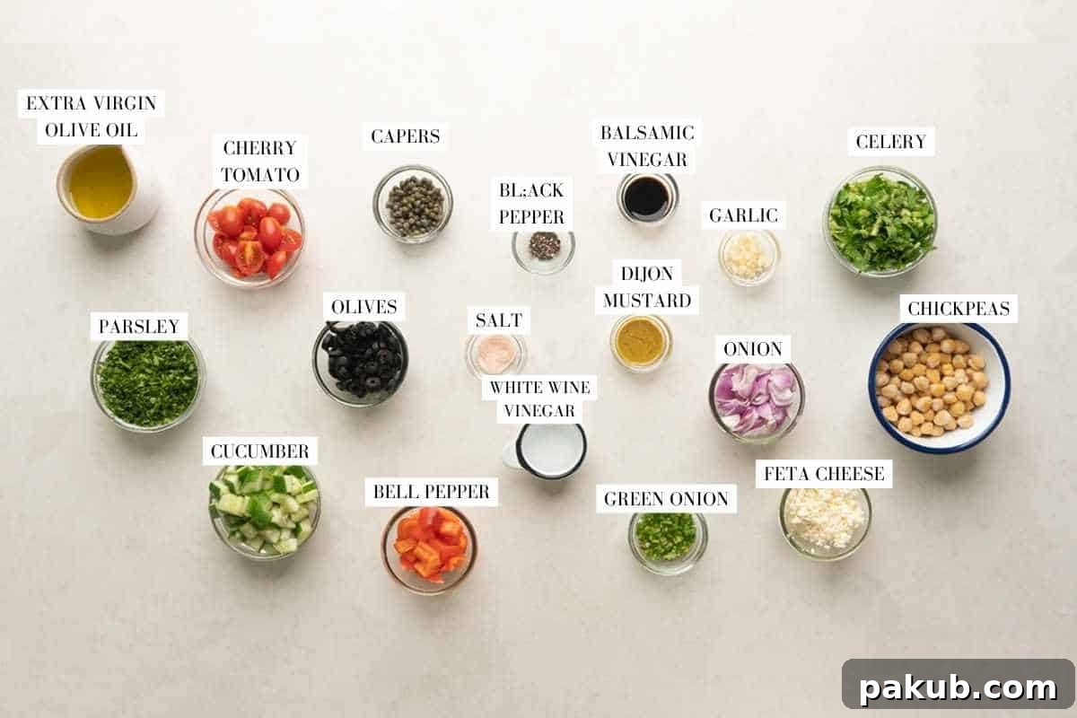 Ingredient shot for Mediterranean chickpea salad, showcasing fresh vegetables, herbs, and dressing components.