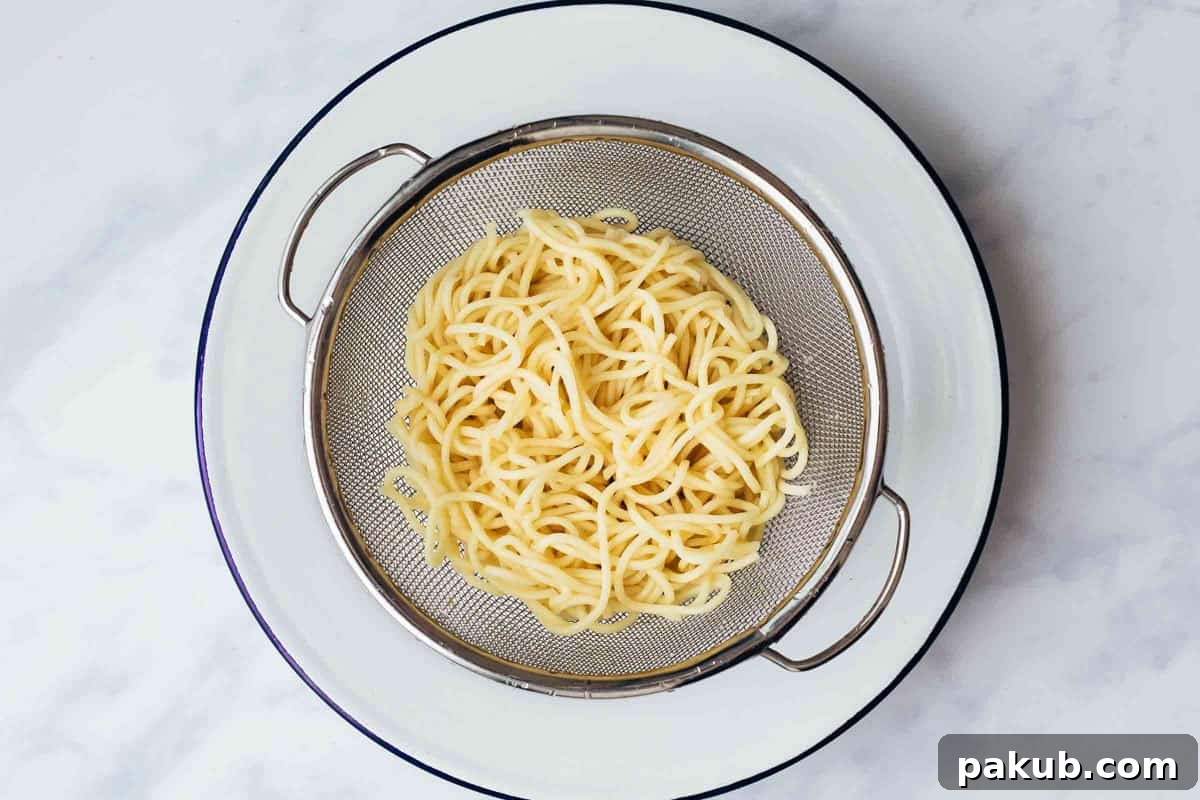 Boiled noodles being drained in a colander and rinsed thoroughly with cold water, a key step for crispy fried noodles