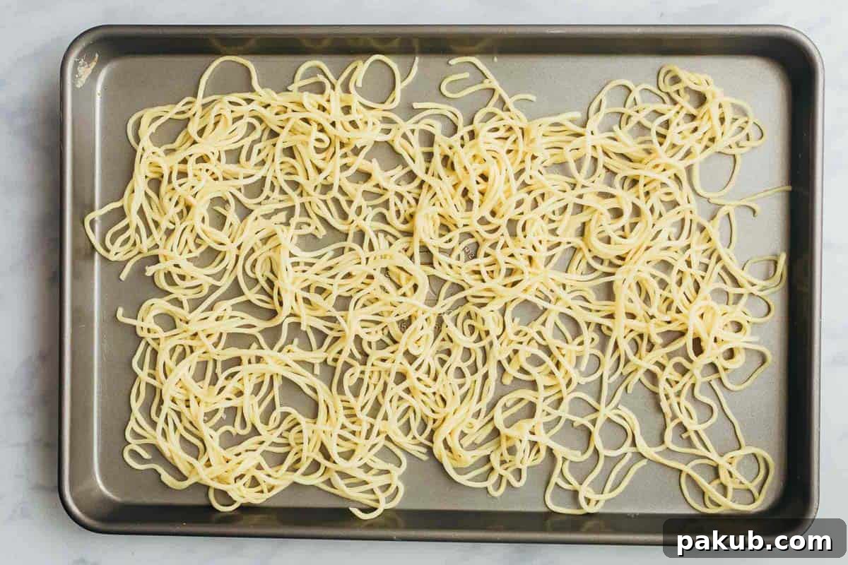 Noodles carefully spread out on a cookie sheet for air drying, an important step before frying to achieve crispy fried noodles