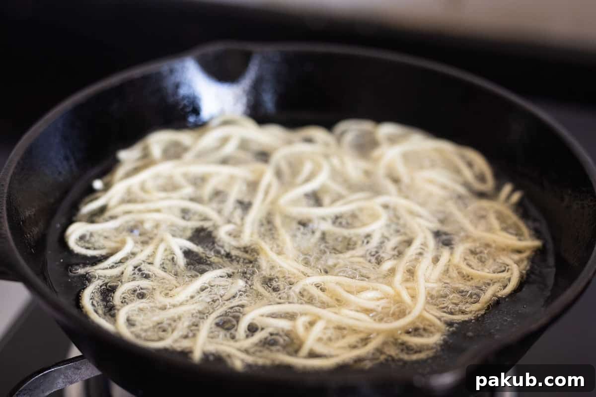 Noodles being deep fried in hot oil until they turn a perfect golden brown, ensuring crispy fried noodles