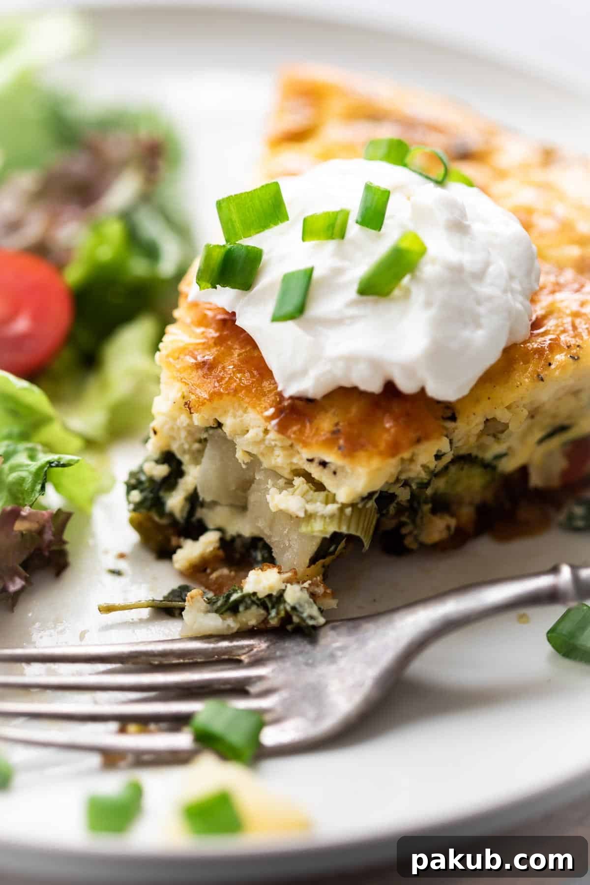 Rustic Cast Iron Spinach Potato Frittata 4 Another enticing slice of Spinach Potato Veggie Frittata, beautifully plated and garnished with a dollop of sour cream and finely chopped green onions, emphasizing its gourmet appeal.