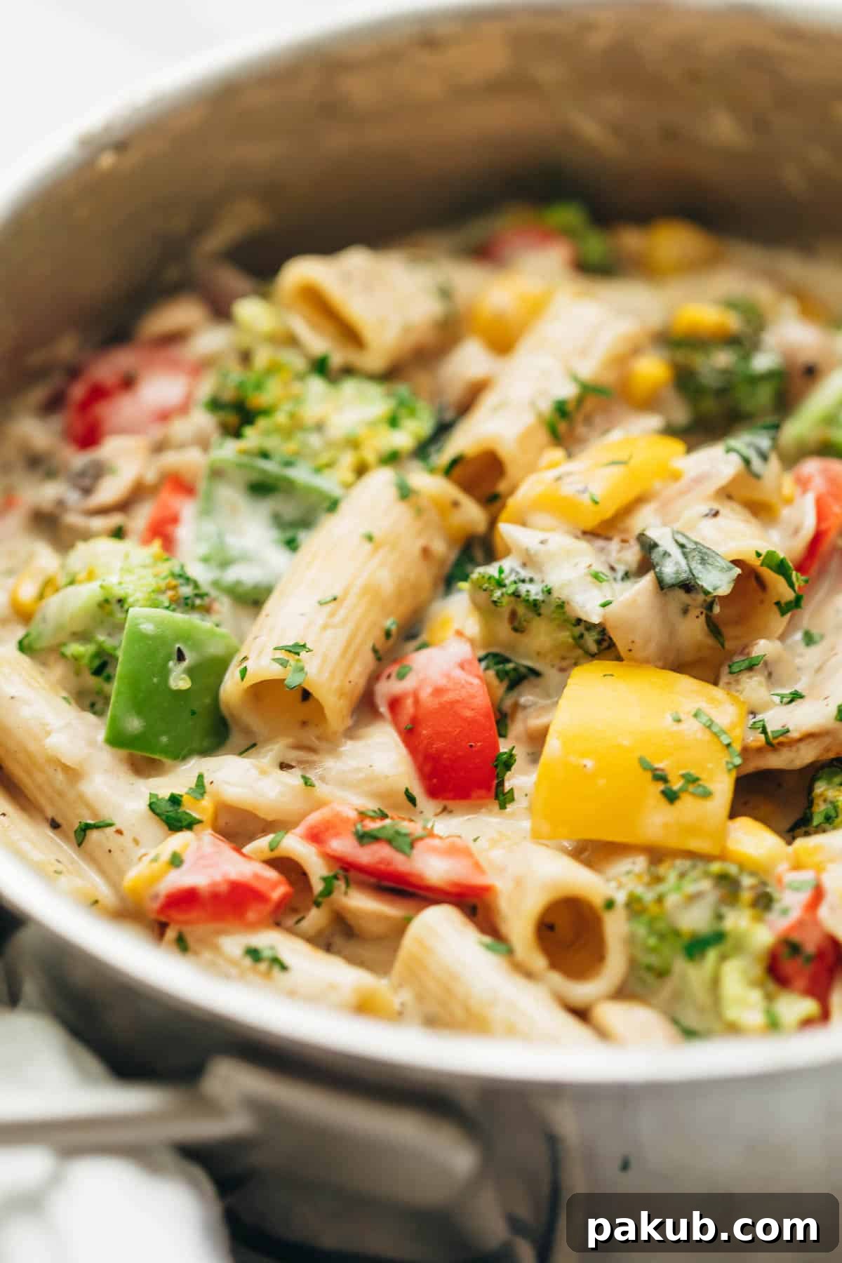 Creamy Garden Vegetable Pasta 3 Close-up of creamy white sauce pasta with various colorful vegetables in a large pan on the stovetop.