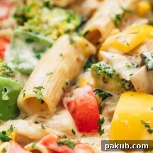 Closeup of white sauce pasta with vegetables, garnished with fresh basil.