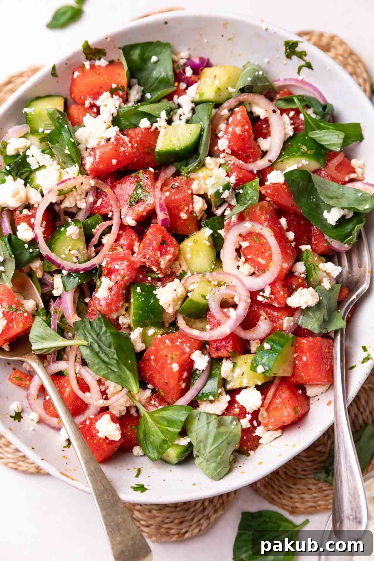 Ultimate Summer Watermelon Salad 2 A vibrant watermelon salad in a white bowl, garnished with fresh herbs, alongside a fork and spoon, ready to be enjoyed.