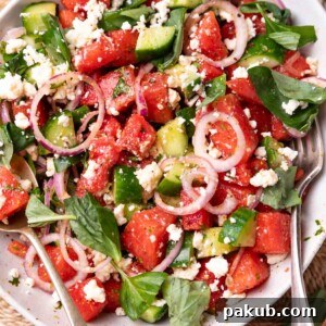 A vibrant watermelon salad in a white bowl with fork and spoon