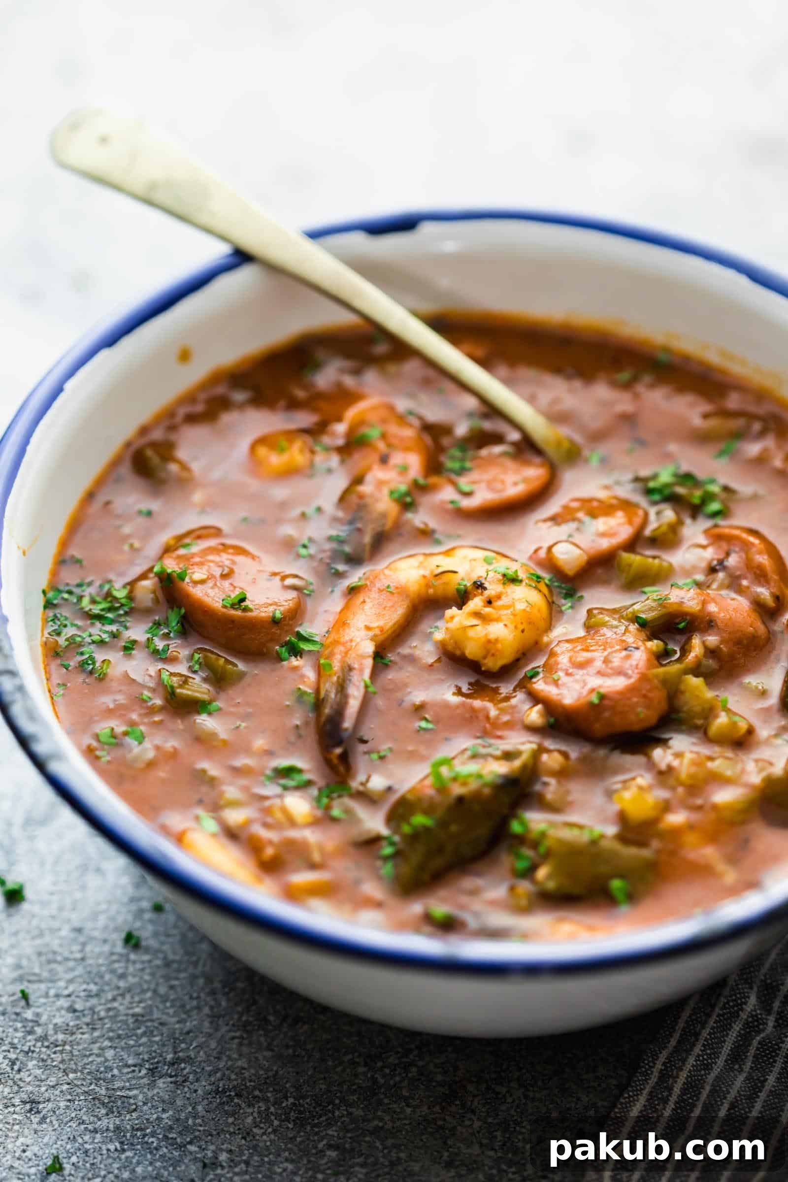 Side angle view of New Orleans Shrimp and Sausage Gumbo in an enamel bowl with a spoon, showing its vibrant colors and inviting presentation.