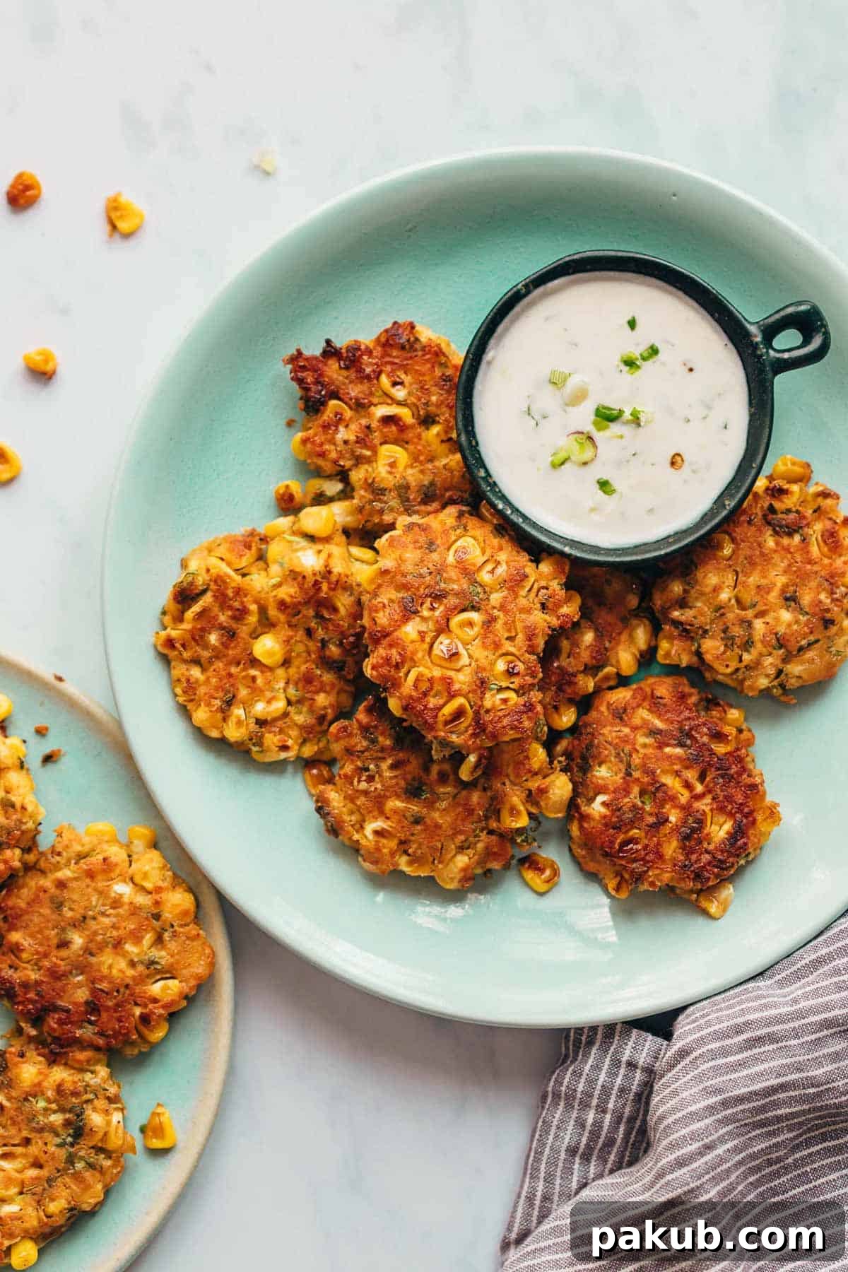 Fiesta-Ready Mexican Corn Fritters in 15 Minutes 3 Mexican corn fritters served on a blue plate with a creamy dip on the side