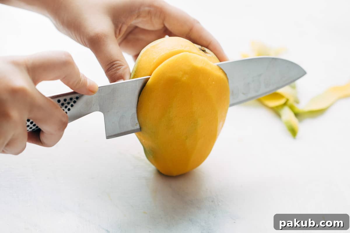 Easy Step-by-Step Guide to Cutting a Mango 11 The two main cheeks of a perfectly peeled mango being precisely cut away from the central pit, ready for further processing.