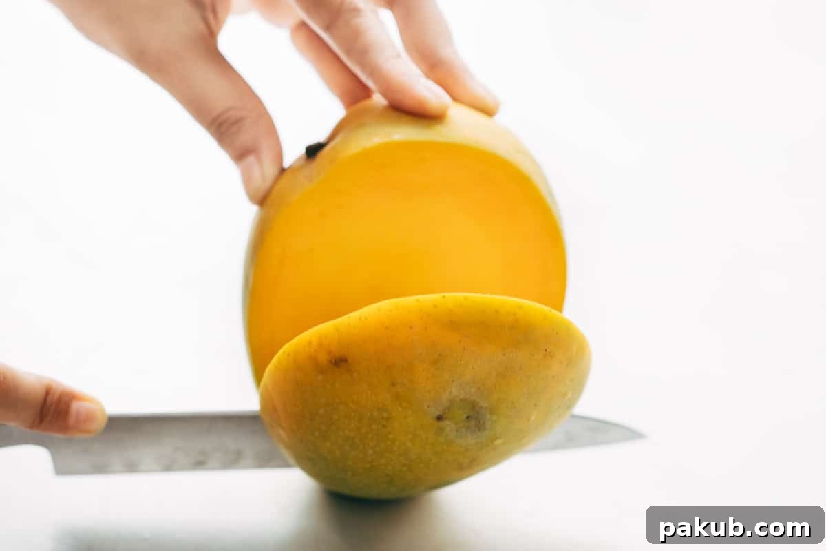 Easy Step-by-Step Guide to Cutting a Mango 4 A sharp knife precisely slicing off one of the succulent cheeks of a ripe mango, carefully avoiding the central pit.