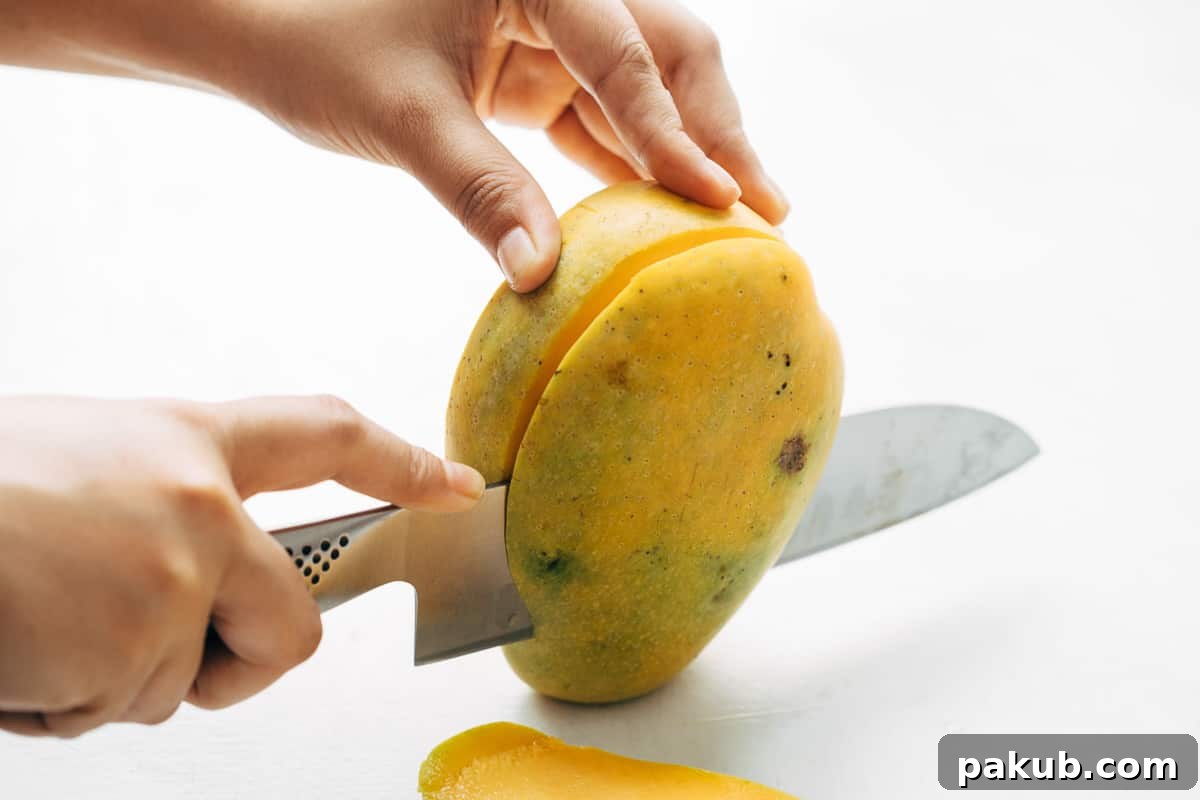 Easy Step-by-Step Guide to Cutting a Mango 5 The second luscious cheek of the mango being expertly sliced away, mirroring the first cut to maximize fruit yield around the pit.